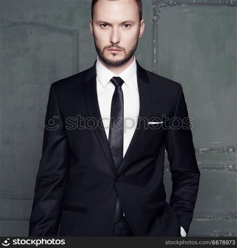 Portrait of handsome stylish man in elegant black suit. Sexy young man in stylish smoking pose in dark studio. Glamour photography of fashionable male model.