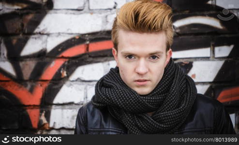 Portrait of handsome trendy man outdoor in city setting, male model stylish haircut against graffiti wall