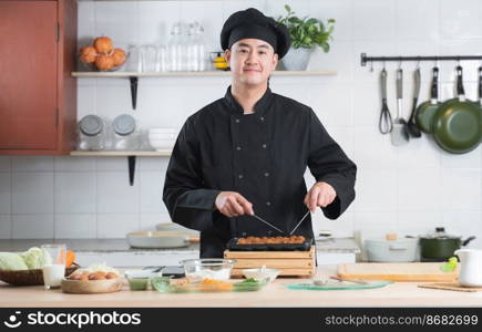 Portrait of handsome young Asian man chef wear black uniform smiling and standing, making japanese food called takoyaki with ingredients on table at kitchen restaurant