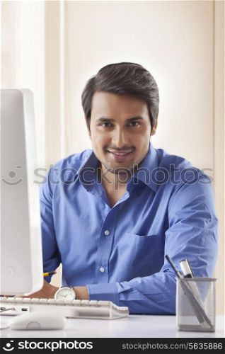 Portrait of handsome young businessman at computer desk in office