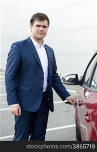 Portrait of handsome young businessman opening car door