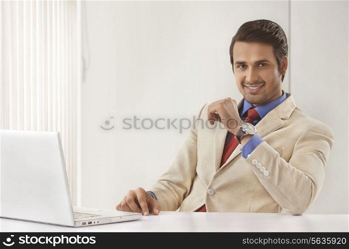 Portrait of handsome young businessman with laptop at office desk