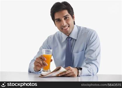 Portrait of handsome young businessman with newspaper and glass of juice over white background