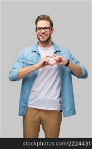 Portrait of handsome young caucasian man making heart sign by hands over grey background.. Portrait of handsome young caucasian man making heart sign by hands over grey background