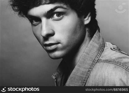 Portrait of Handsome Young Man. A Men in a Denim Jacket Posing on a Gray Background. Black and White Photo