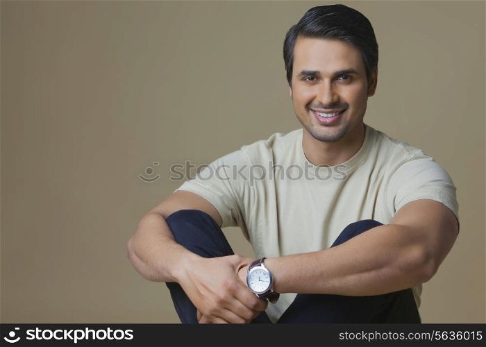 Portrait of handsome young man hugging knees over colored background