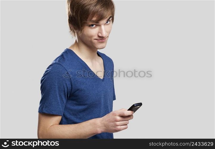 Portrait of handsome young man sending text messages with is mobile phone, over a gray background