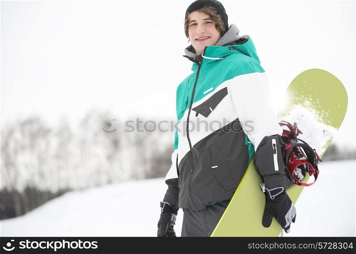 Portrait of handsome young man with snowboard in snow