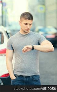 Portrait of handsome young muscular man looking on his wrist watch in urban context