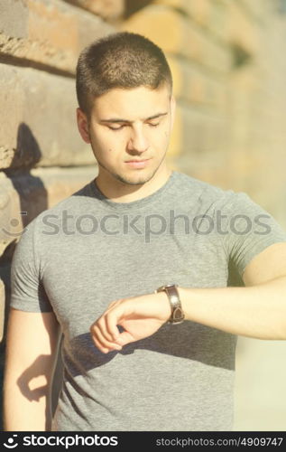 Portrait of handsome young muscular man looking on his wrist watch in urban context