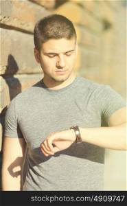 Portrait of handsome young muscular man looking on his wrist watch in urban context