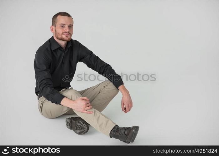 Portrait of handsome young thoughtful man sitting on white background, full length