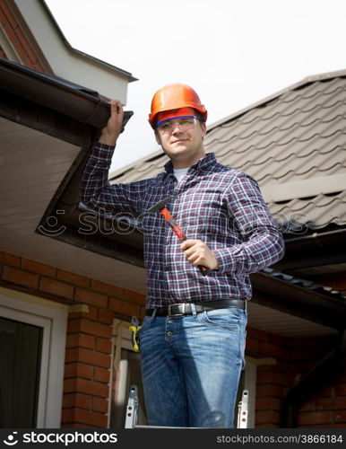 Portrait of handyman standing on high ladder and inspecting house roof