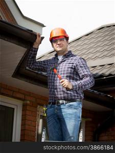 Portrait of handyman standing on high ladder and inspecting house roof
