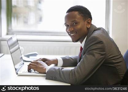 Portrait of happy African American businessman using laptop at office desk