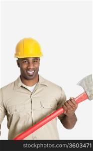 Portrait of happy African male construction worker holding axe over gray background