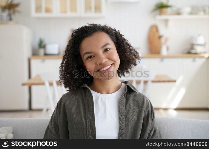 Portrait of happy afro girl at home. Young african american woman among modern scandinavian interior in her room. Trendy curly hairstyle, optimistic smile and attractive appearance. Positive emotions.. Portrait of happy afro girl at home. Curly hairstyle, optimistic smile and positive emotions.