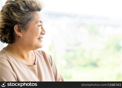 Portrait of happy and smile elderly senior adult female standing beside window in domestic living room - recovery and rehabilitation concept