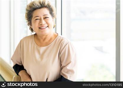 Portrait of happy and smile elderly senior adult female standing beside window in domestic living room - recovery and rehabilitation concept