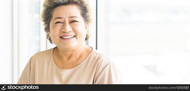 Portrait of happy and smile elderly senior adult female standing beside window in domestic living room - recovery and rehabilitation concept. web banner panoramic.