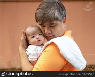 Portrait of happy Asia father holding his newborn sweet baby dressed in white clothes. The father embracing his baby with love and care. his daughter always happy when he is held.