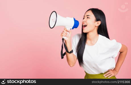 Portrait of happy Asian beautiful young woman teen confident smiling face holding making announcement message shouting screaming in megaphone, studio shot isolated on pink background, with copy space