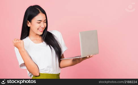 Portrait of happy Asian beautiful young woman teen confident smiling face holding using laptop computer and excited celebrating success, studio shot isolated on pink background, with copy space