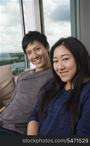 Portrait of happy Asian couple sitting on sofa at home