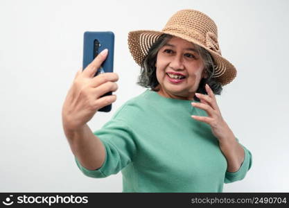 Portrait of happy Asian senior woman wearing sunglasses, a hat, and holding smartphone for a selfie, standing isolated on white background. Concept of tourist enjoy and fun valentine day after retire