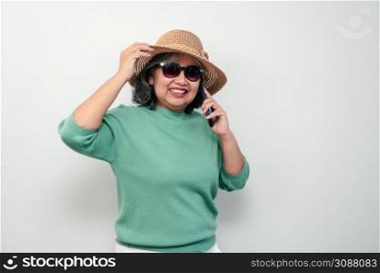 Portrait of happy asian senior woman wearing sunglasses, a hat, and holding smartphone standing isolated on white background. Concept of tourist enjoy and fun valentine day after retire