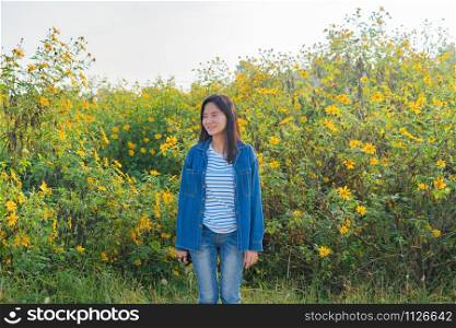 Portrait of happy Asian woman enjoying and relaxing at Tree Marigold or yellow flowers national garden park during travel holidays vacation trip outdoors at Mae Moh, Lumpang, Thailand. Lifestyle.