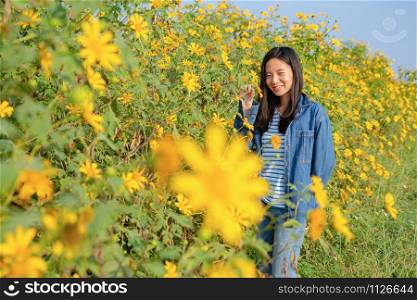 Portrait of happy Asian woman enjoying and relaxing at Tree Marigold or yellow flowers national garden park during travel holidays vacation trip outdoors at Mae Moh, Lumpang, Thailand. Lifestyle.