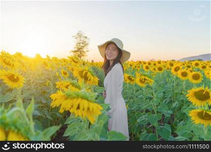 Portrait of happy Asian woman enjoying and relaxing in a full bloom sunflower field during travel holidays vacation trip outdoors at natural garden park at noon in Lopburi, Thailand. Lifestyle.