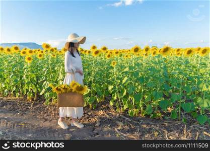 Portrait of happy Asian woman enjoying and relaxing in a full bloom sunflower field during travel holidays vacation trip outdoors at natural garden park at noon in Lopburi, Thailand. Lifestyle.