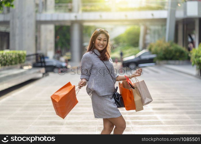 Portrait of Happy Asian woman walking and holding the shopping bag in downtown around shopping center, fashion concept