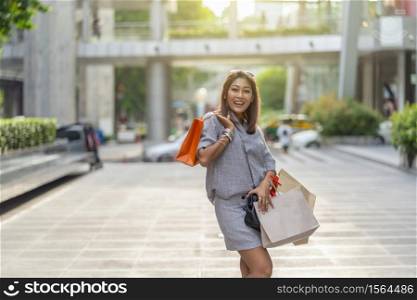 Portrait of Happy Asian woman walking and holding the shopping bag in downtown around shopping center, fashion concept
