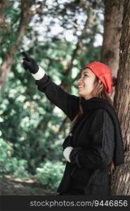 Portrait of Happy Asian young woman in winter costume pointing aside at the forest. Vacation and travel concept.