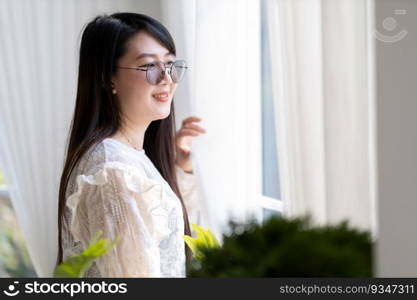 Portrait of Happy Attractive asian people cute woman wearing white lace shirt with the curtains on the window in the room felt like relaxing in house like the background