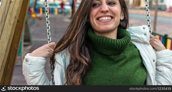 Portrait of Happy attractive hispanic woman playing swinging. hipster style. Cute long hair girl swinging and smiling.. Portrait of Happy attractive hispanic girl playing at a swing set.