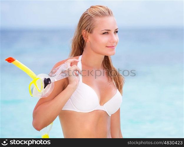 Portrait of happy beautiful girl standing on seashore with a diving mask in hand, having fun on the beach, enjoying summer watersport