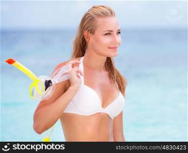Portrait of happy beautiful girl standing on seashore with a diving mask in hand, having fun on the beach, enjoying summer watersport
