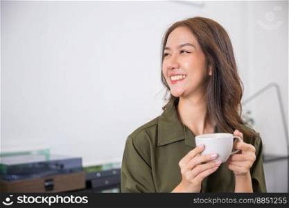 Portrait of Happy beautiful woman rest in summer after wakeup at office room, Asian young woman hands holding hot coffee or tea cup for drink in morning while posing, white porcelain mug mock up