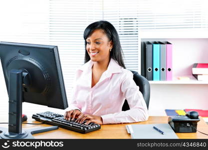 Portrait of happy black business woman at desk typing on computer