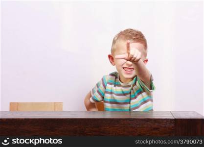 Portrait of happy blond cute boy child kid showing pointing at you at the table interior. Emotions.
