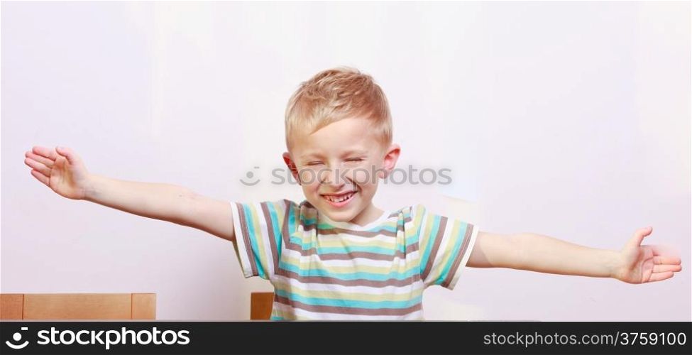 Portrait of happy blond cute boy child kid with arms open at the table interior. Emotions.