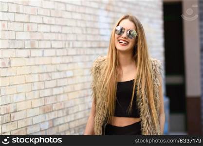 Portrait of happy blonde girl smiling in urban background wearing round sunglasses