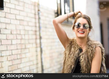 Portrait of happy blonde girl smiling in urban background wearing round sunglasses