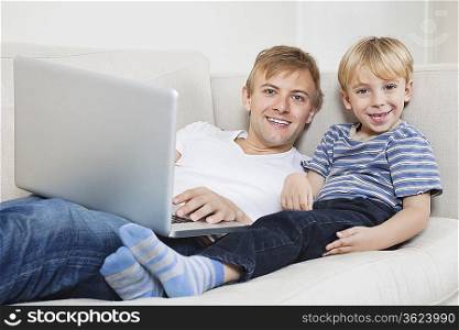 Portrait of happy boy with father using laptop on sofa