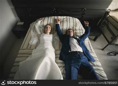 Portrait of happy bride and groom lying on bed at hotel room