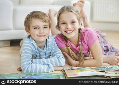Portrait of happy brother and sister with story books while lying on floor